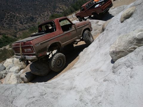 1978 Ford Bronco - A red 1978 Ford Bronco navigates a rocky incline, with another red pickup truck following closely behind.