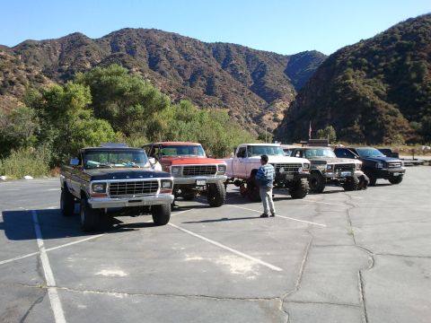 1978 Ford Bronco - A group of Ford trucks and SUVs are parked in a lot with a mountainous backdrop.