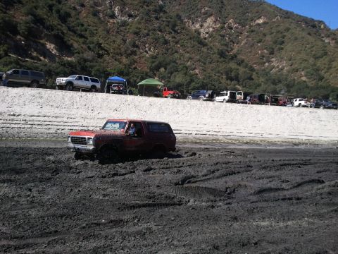 1978 Ford Bronco - A 1978 Ford Bronco navigates a muddy terrain, with several other vehicles visible on the embankment above.
