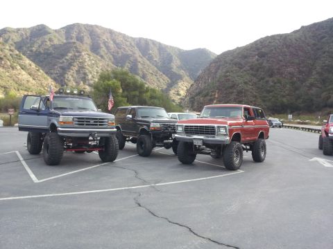 1978 Ford Bronco - Several modified SUVs are parked in a lot, with a mountainous backdrop. The red SUV on the right appears to be a 1978 Ford Bronco.