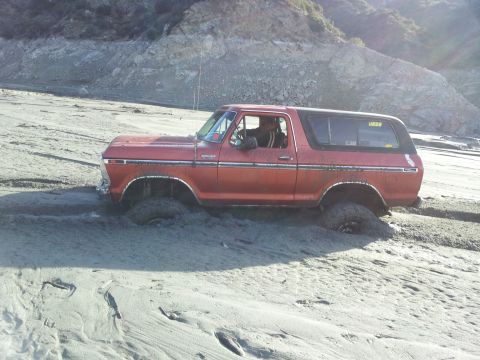 1978 Ford Bronco - A red 1978 Ford Bronco is stuck in thick mud, with its tires partially submerged.