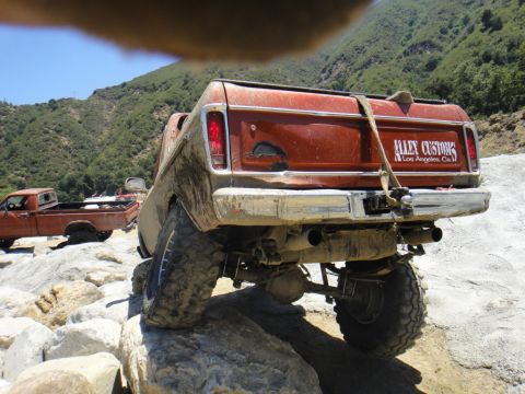 1978 Ford Bronco - Muddy pickup truck navigating rocky terrain, with a second truck in the background.