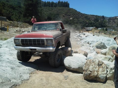 1978 Ford Bronco - This lifted 1978 Ford Bronco is shown off-roading over large rocks on a sunny day.