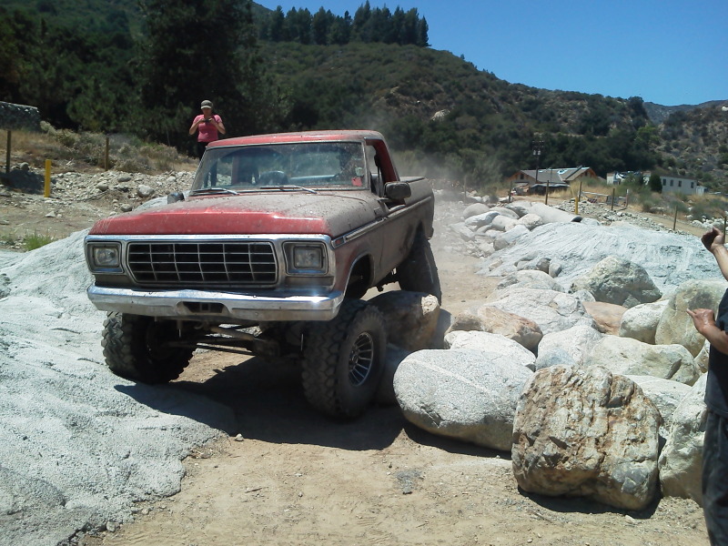 Red 1978 Ford Bronco with lifted suspension navigating a rocky terrain