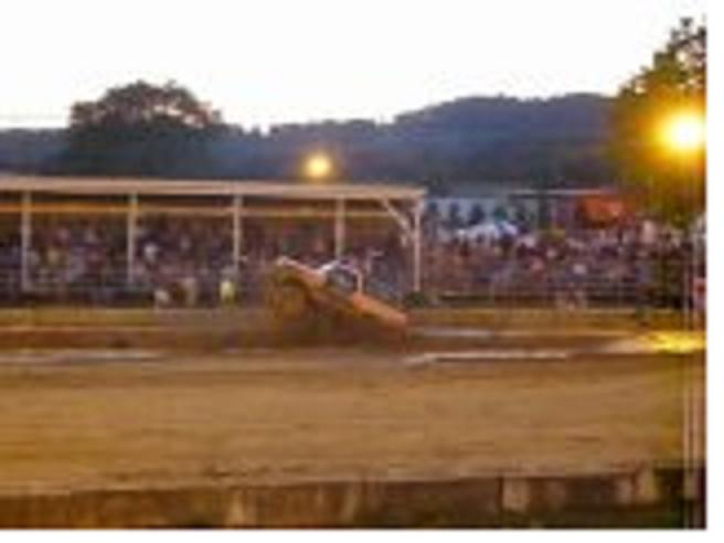 Mud bogging truck kicking up dirt on a track with spectators in the background