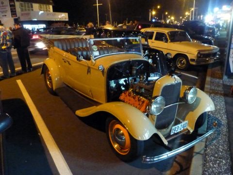 1969 Lincoln Continental - A tan convertible hot rod with its hood open, revealing the engine. Other vehicles are parked nearby.