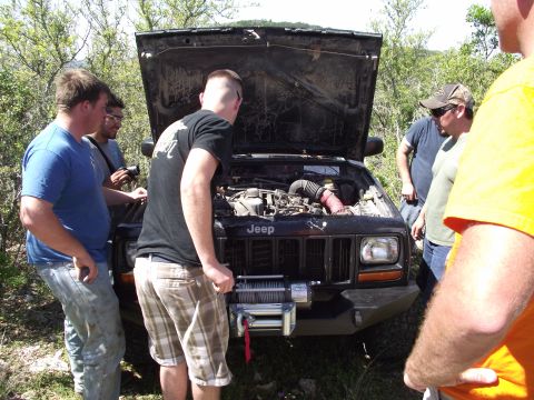 1989 Ford Bronco - A group of men examine the engine of a Jeep Cherokee XJ equipped with a front winch.
