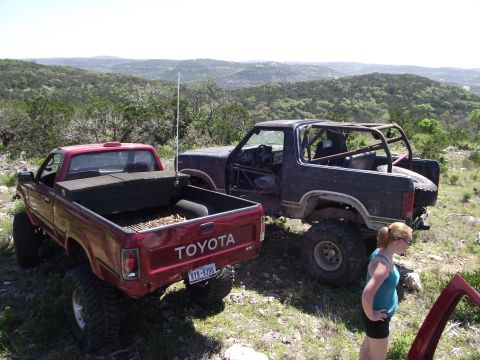 1989 Ford Bronco - Two modified off-road vehicles are parked on a hillside with a scenic view of rolling hills.