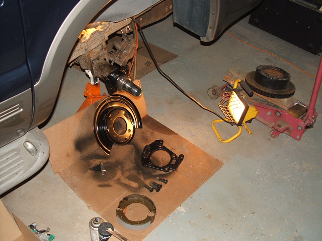Ford Excursion brake parts laid out on cardboard, vehicle on jack stands