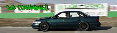 1995 Ford Taurus - A dark green sedan with black wheels is seen in profile on a race track, with a billboard in the background.