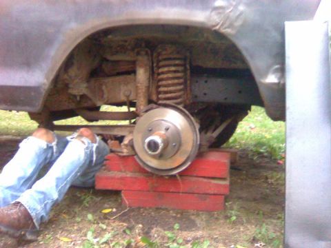 1979 Ford Bronco - A person works on the suspension of a 1979 Ford Bronco, which is supported by red blocks.