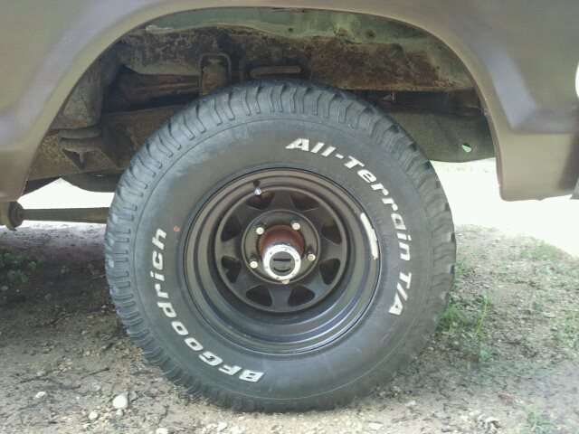 Brown vehicle's rear wheel with BFGoodrich All-Terrain T/A tire and black rim, showing rust on the undercarriage