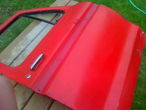1979 Ford Bronco - Red vehicle door with chrome handle and vent window, placed on wooden planks outdoors.