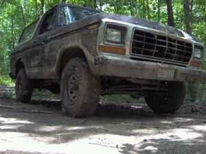 1979 Ford Bronco - A muddy 1978 Ford Bronco navigates a wooded trail.