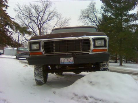 1979 Ford Bronco - A Ford truck sits in the snow, its grille and headlights prominent. A second vehicle is visible in the background.