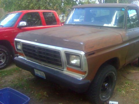 1979 Ford Bronco - A weathered 1978 Ford Bronco sits beside a red truck, its front grille and headlights visible.