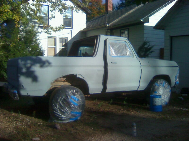 1979 Ford Bronco in primer with wheels covered, parked outside a house