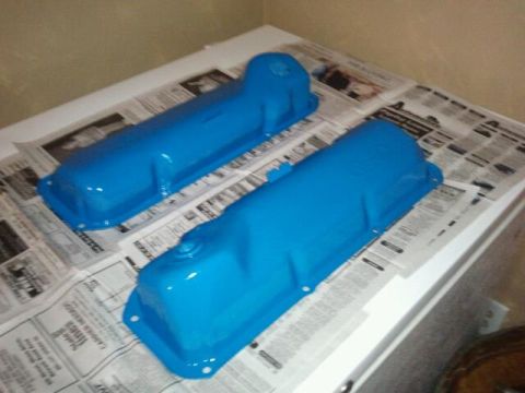 1979 Ford Bronco - Two freshly painted blue valve covers are drying on a surface covered with newspaper.