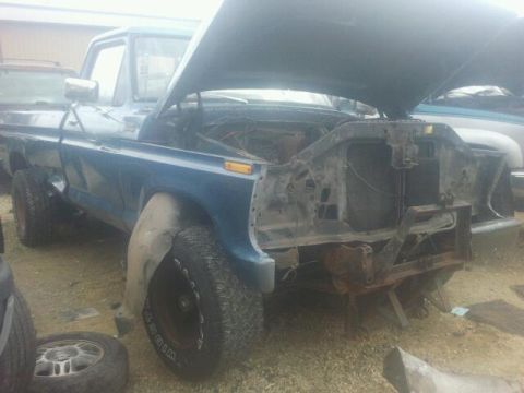 1979 Ford Bronco - This blue pickup truck has its hood up and the front end is missing parts.