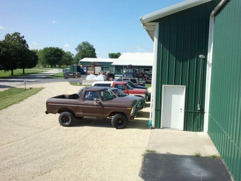 1979 Ford Bronco - A brown pickup truck is parked beside a green metal building on a sunny day.