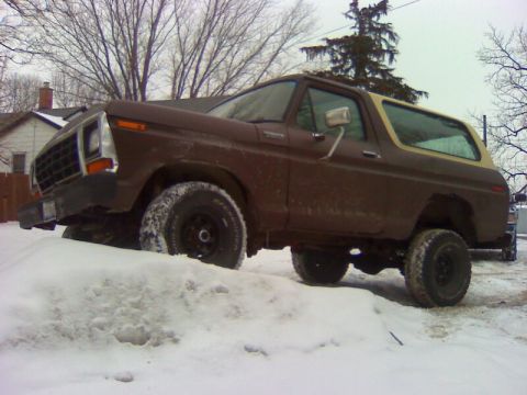 1979 Ford Bronco - A brown Ford Bronco with a tan top is partially buried in snow, with its front end angled upwards.