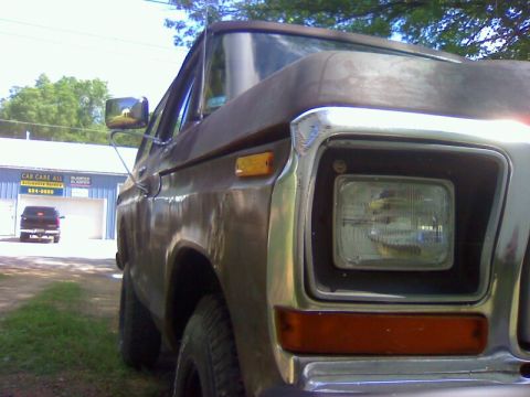1979 Ford Bronco - A weathered 1978 Ford Bronco is parked outside a repair shop, with another vehicle in the distance.