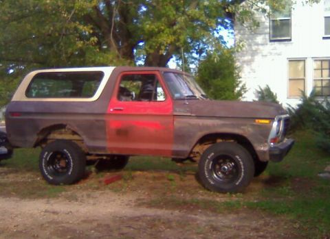 1979 Ford Bronco - This weathered Ford Bronco sits parked outdoors, showing its distinct two-tone paint and lifted suspension.