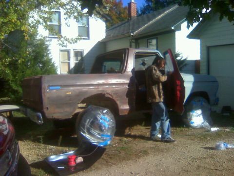 1979 Ford Bronco - A man works on a weathered 1973 Ford F-100 pickup truck in a yard, with its wheels covered for protection.