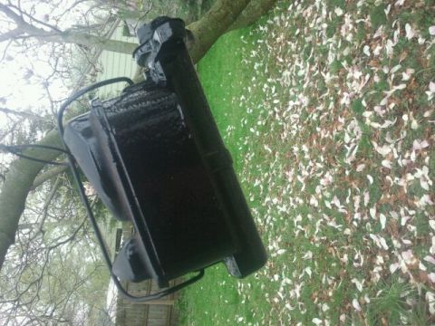 1979 Ford Bronco - A black painted automotive part is shown resting on the grass, suspended by a metal frame.