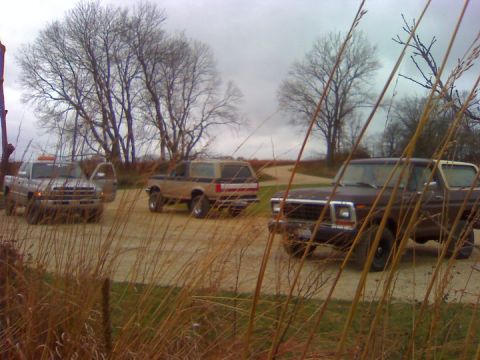 1979 Ford Bronco - Several older model SUVs and a pickup truck are parked on a dirt road under an overcast sky.