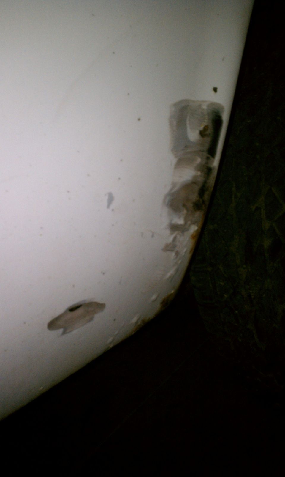 Close-up of white body panel with sanded bodywork, rust and a hole near the wheel opening