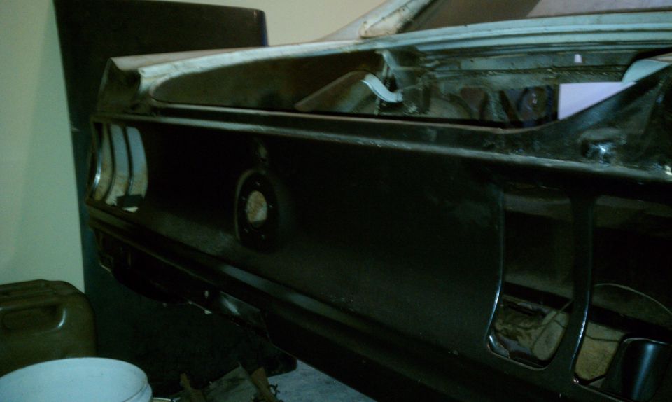 Rear tail panel of black-primered Mustang body shell in garage, fuel filler hole and taillight openings visible