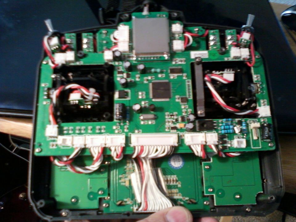 Opened RC transmitter showing green circuit board, gimbals, and wiring harnesses