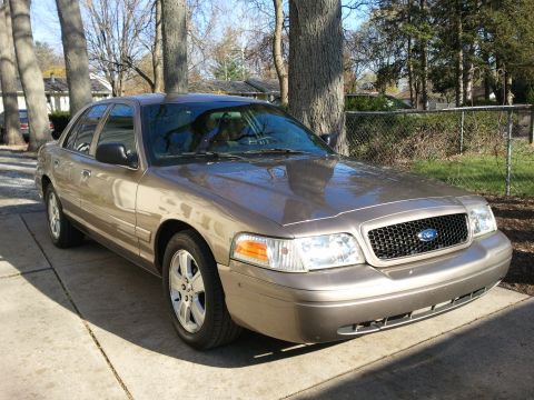 2007 Ford Crown Victoria - A tan 2007 Ford Crown Victoria is parked on a driveway, showing its distinctive honeycomb grille and front end.
