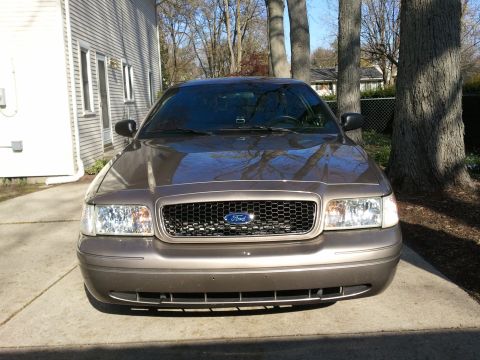 2007 Ford Crown Victoria - A brown Ford Crown Victoria is parked in a driveway with a house and trees in the background.