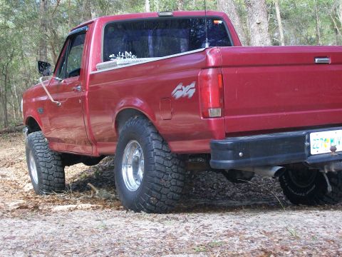 1993 Ford F-150 - A red pickup truck is parked on a dirt path surrounded by trees. The truck has a 4x4 decal on its side.