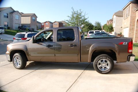 2007 GMC Sierra 1500 - A brown GMC Sierra pickup truck is parked in a suburban driveway with other vehicles visible.