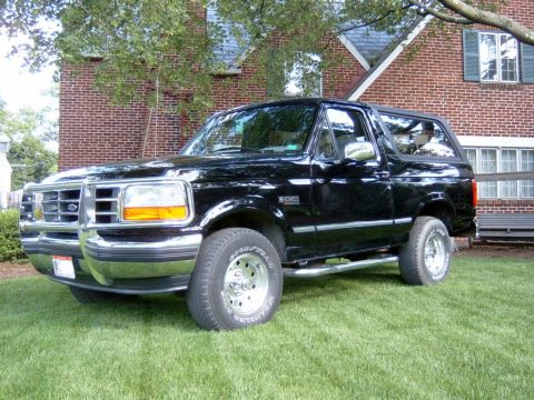 1995 Ford Bronco - This black 1995 Ford Bronco is shown from a three-quarter front view, parked on a lawn with a brick house in the background.