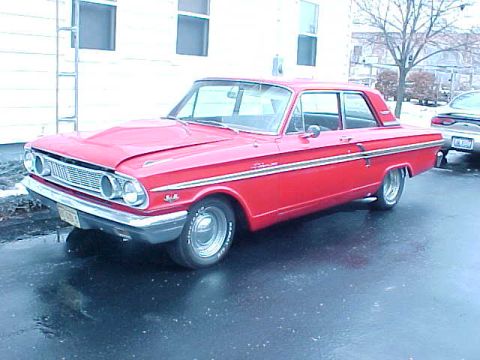 1969 Ford Torino - A red 1964 Ford Falcon sedan is parked on a wet surface, with another vehicle visible in the background.