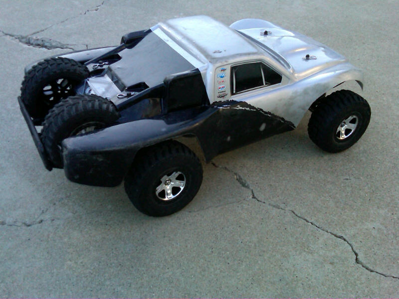 Silver and black remote control monster truck with large tires, parked on cracked concrete