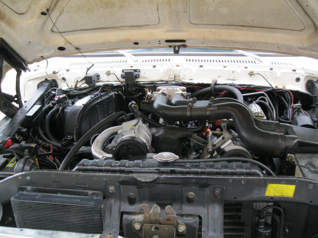 Engine bay of a white vehicle with complex wiring and hoses, showing the radiator and air intake system