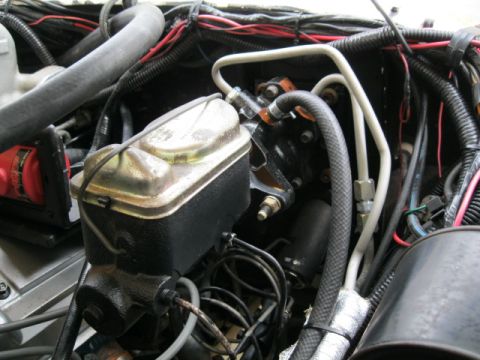 1978 Ford Bronco - Close-up view of the brake master cylinder and plumbing in an engine compartment.