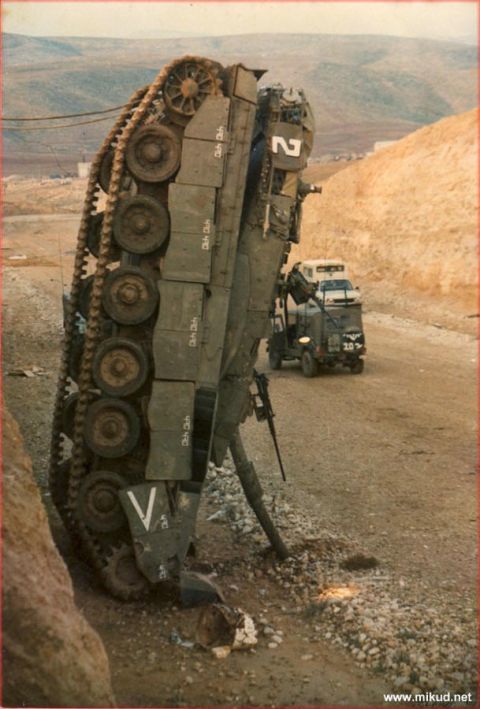1978 Ford Bronco - An overturned military tank lies on its side next to a dirt road, with a military truck visible in the distance.