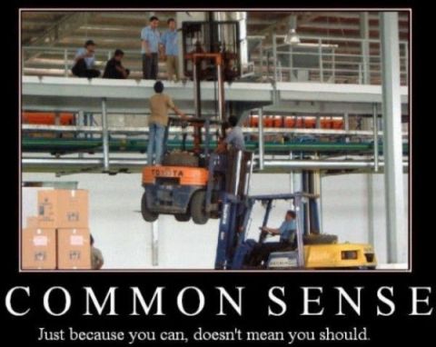 1978 Ford Bronco - A precarious situation unfolds in a warehouse as one forklift lifts another, with onlookers observing.