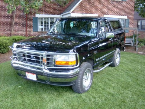 1995 Ford Bronco - This black Ford Bronco, likely from the early to mid-1990s, is parked on a lawn in front of a brick house.
