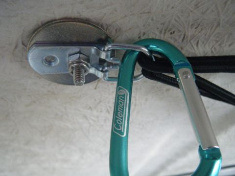 2003 Nissan Frontier - A close-up view of a green Coleman carabiner clip secured by a metal bracket and bolt.