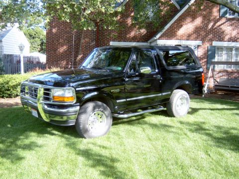 1995 Ford Bronco - A black 1995 Ford Bronco is shown from a three-quarter front view, parked on a grassy lawn in front of a brick house.