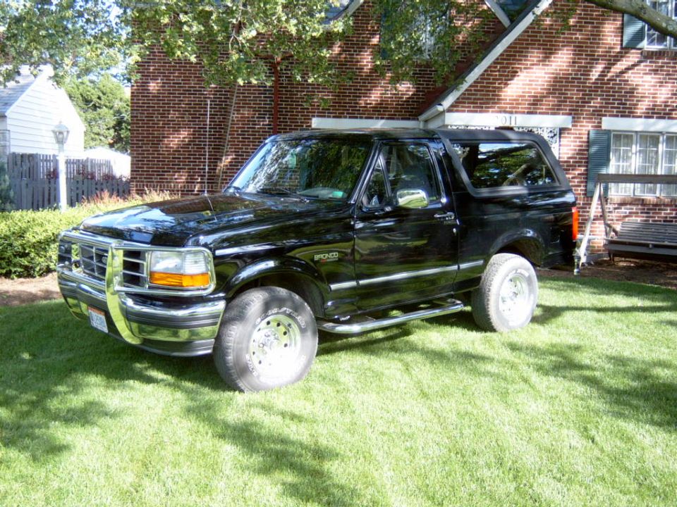 Black Ford Bronco SUV parked on lawn by brick house, driver-side 3/4 front view