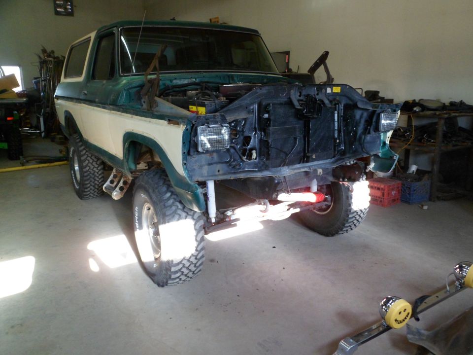 Green and white 1979 Ford Bronco front view, hood open, in garage