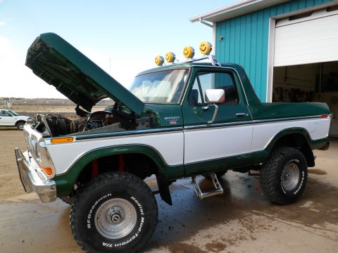1979 Ford Bronco - This classic Ford Bronco is parked outside a garage with its hood up, revealing the engine bay.